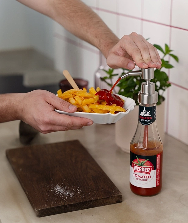 Mann gibt Ketchup auf Pommes aus einer Flasche mit Pumpe.