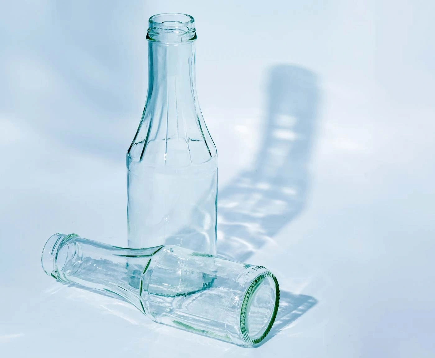 Zwei leere Glasflaschen mit Schatten auf hellem Hintergrund.