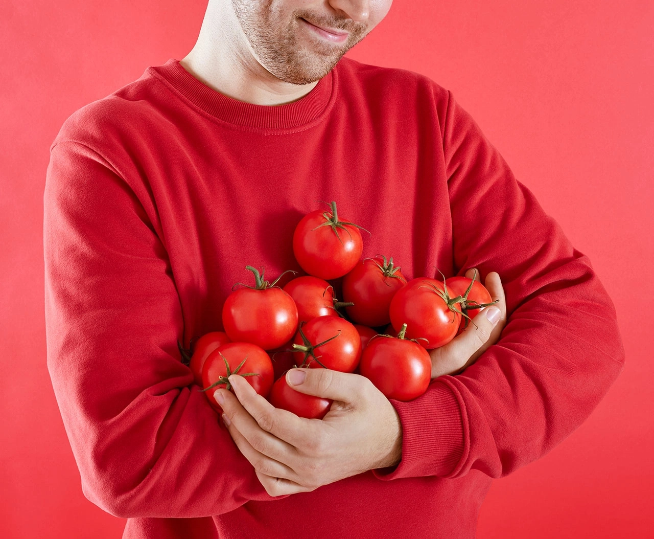 Mann mit roten Tomaten im roten Pullover auf rotem Hintergrund