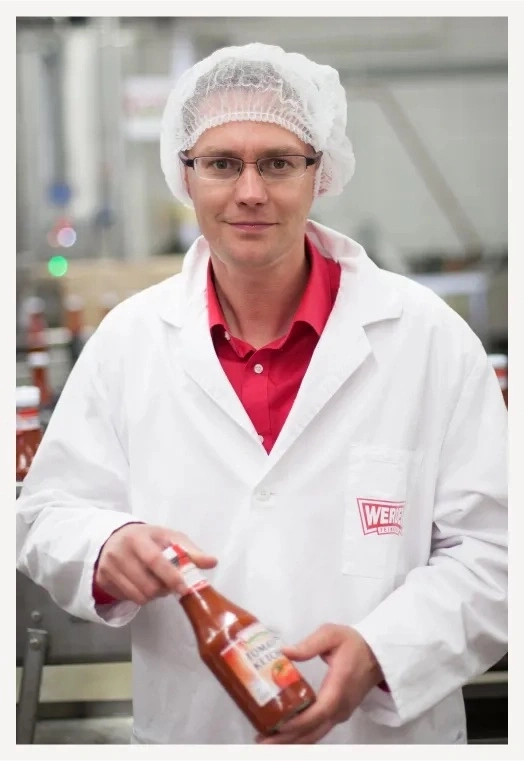 Mann im weißen Kittel mit Haube hält eine Flasche Ketchup