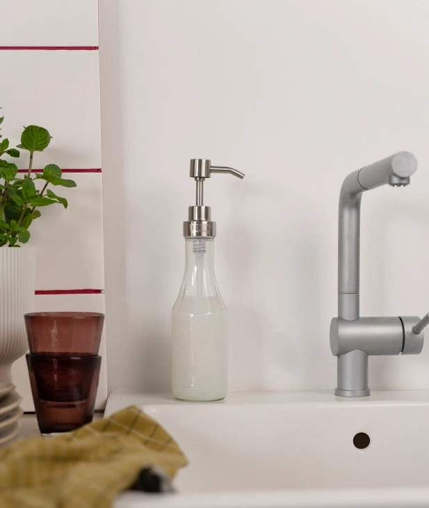 Ein Seifenspender aus Glas neben einer Küchenspüle mit Wasserhahn.