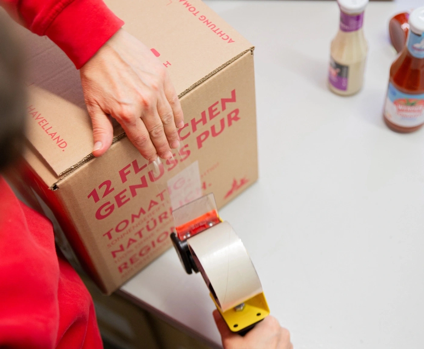 Person verpackt Karton mit Tomatenprodukten und Gewürzen.