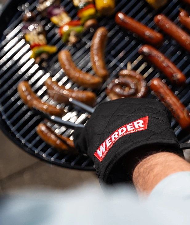 Grillhandschuh mit "Werder"-Logo auf einem Grill mit Würstchen und Gemüse.