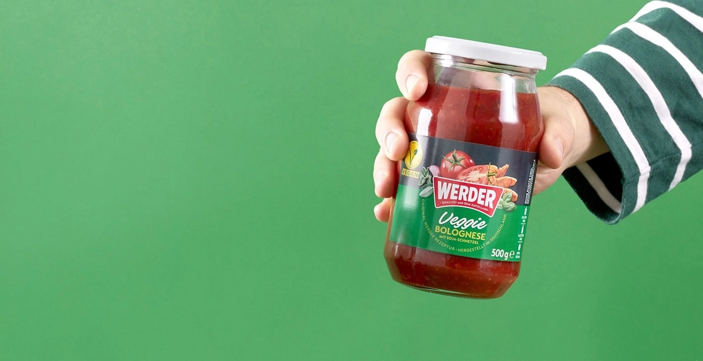 Hand hält ein Glas Werder Veggie Bolognese mit Soja-Schnitzel