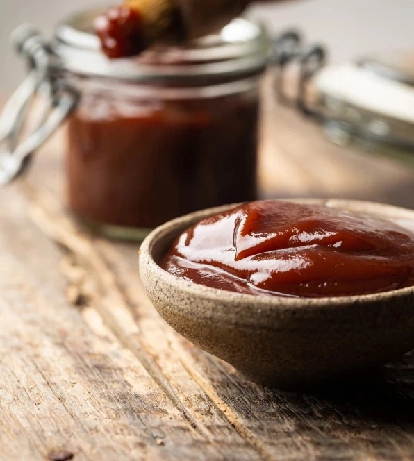 Ein Glas und eine Schüssel mit BBQ-Sauce auf Holzoberfläche