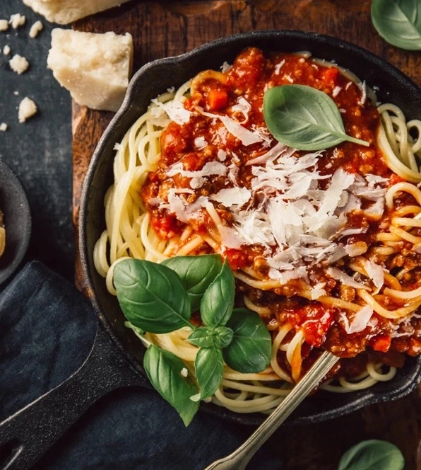 Spaghetti Bolognese in einer Pfanne mit Parmesan und Basilikum, nah aufgenommen.