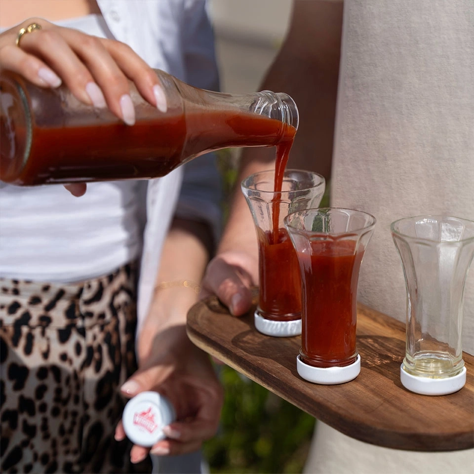 Ein Mann gießt Tomatensaft in kleine Gläser auf einem Holztablett.
