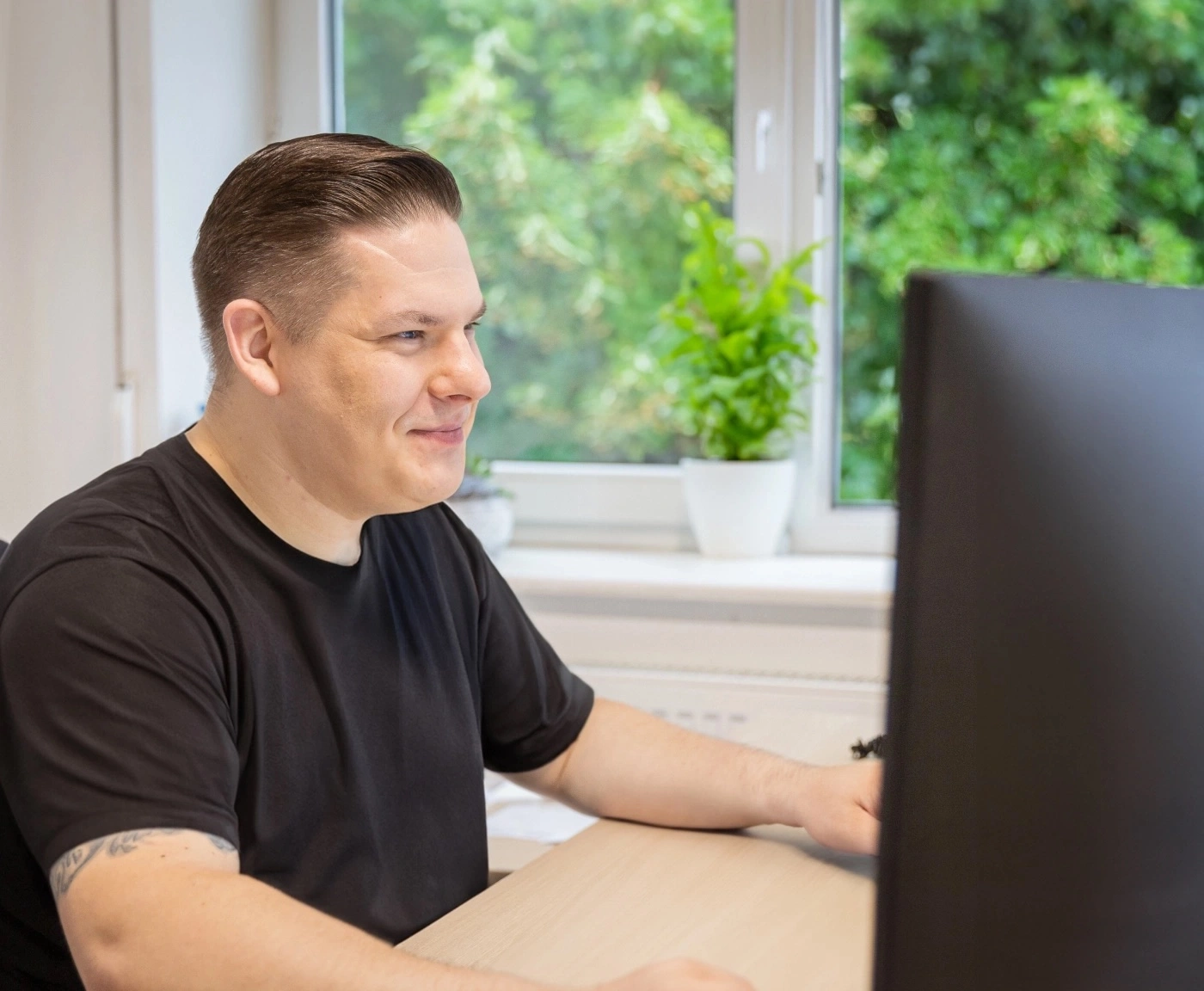 Ein Mann im schwarzen T-Shirt sitzt vor einem Computer