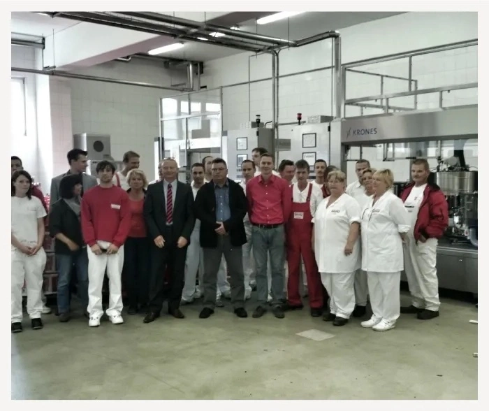 Eine Gruppe von Arbeitern steht in einer Produktionshalle, einige in weißer Arbeitskleidung.